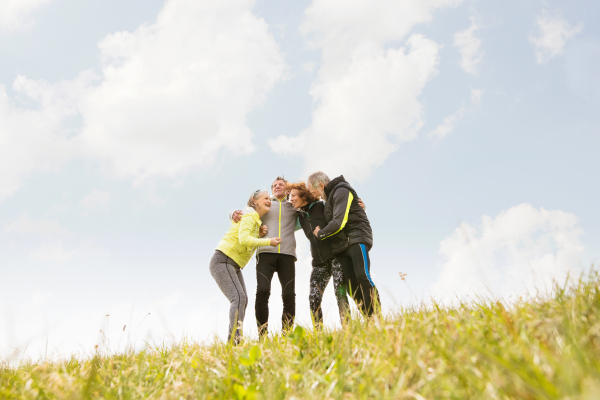 Group of active senior runners outdoors resting, holding around arms.