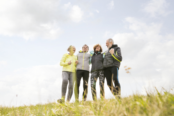 Group of active senior runners outdoors resting, holding around arms.