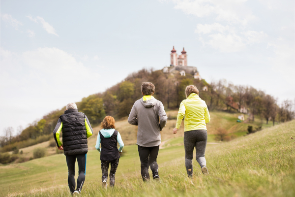 Group of active seniors running together outside on the green hills. Rear view. Calvary in Banska Stiavnica, Slovakia.