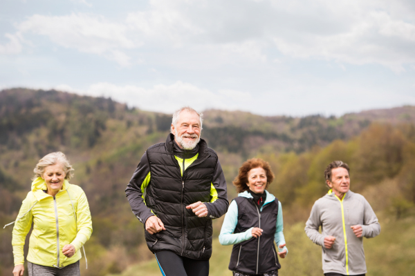 Group of active seniors running together outside on the green hills.