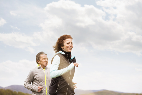 Beautiful active senior couple running outside on green hills.