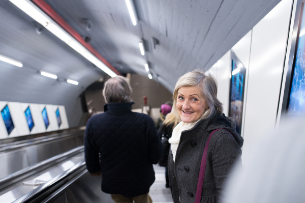 Beautiful senior woman in black coat and white woolen scarf standing at the escalator in Vienna subway