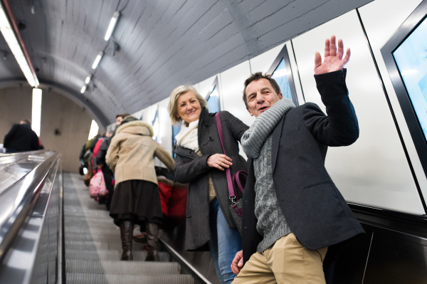 Beautiful senior couple in winter clothes standing at the escalator in Vienna subway, waving