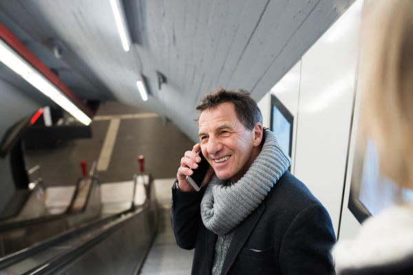 Senior man in winter clothes holding a smart phone, making a phone call, standing at the escalator in Vienna subway