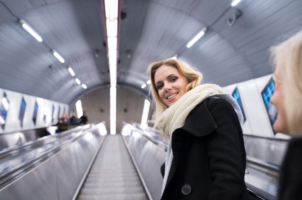 Beautiful young blonde woman in black coat and big woolen scarf standing at the escalator in Vienna subway