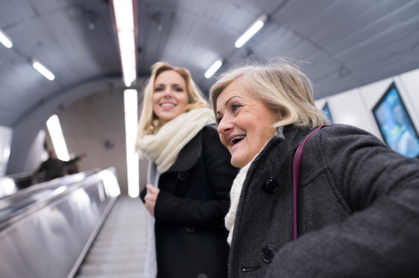 Two beautiful blonde women in black coats and big woolen scarfs standing at the escalator in Vienna subway