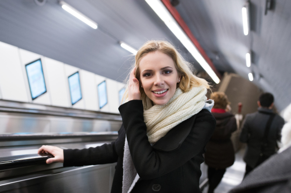 Beautiful young blonde woman in black coat and big woolen scarf standing at the escalator in Vienna subway