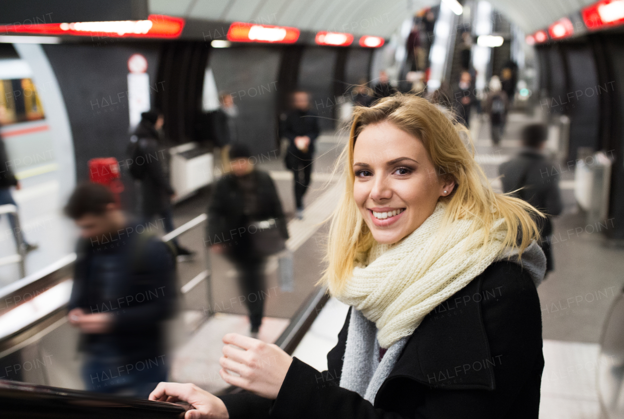 Beautiful young blonde woman in black coat and big woolen scarf standing at the escalator in Vienna subway