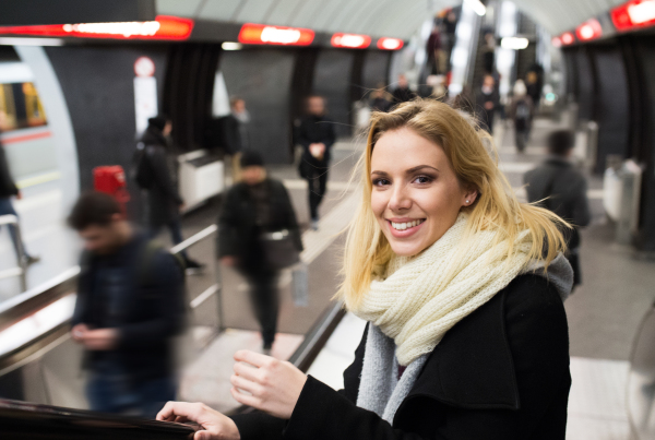 Beautiful young blonde woman in black coat and big woolen scarf standing at the escalator in Vienna subway