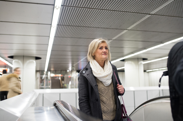 Beautiful senior woman in black coat and white woolen scarf standing at the escalator in Vienna subway