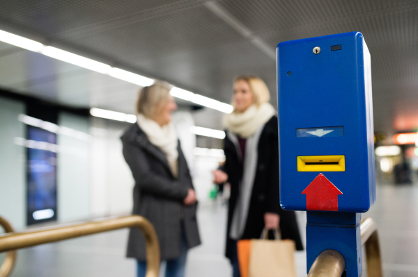 Railway or underground entrance to the station with turnstile. Two unrecognizable women with shopping bags talking.