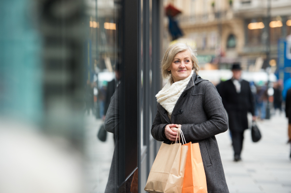 Beautiful senior woman in black coat and woolen scarf window shopping in historical centre of the city of Vienna, Austria. Winter.