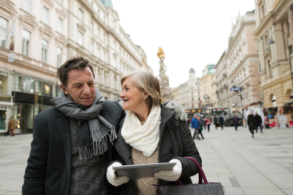 Beautiful senior couple with tablet on a walk in historical centre of the city of Vienna, Austria. Winter.