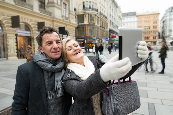 Beautiful senior couple on a walk in historical centre of the city of Vienna, Austria, taking selfie of them with tablet. Winter.