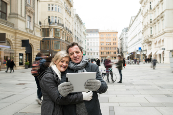 Beautiful senior couple on a walk in historical centre of the city of Vienna, Austria, taking selfie of them with tablet. Winter.