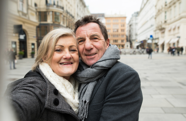 Beautiful senior couple in winter clothes on a walk in historical centre of the city of Vienna, Austria. Woman taking selfie.