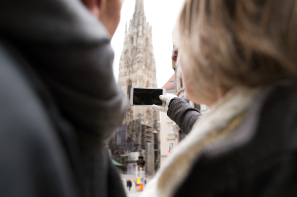 Unrecognizable senior couple on a walk in historical centre of the city of Vienna, Austria. Woman taking selfie of them with smart phone. Winter.