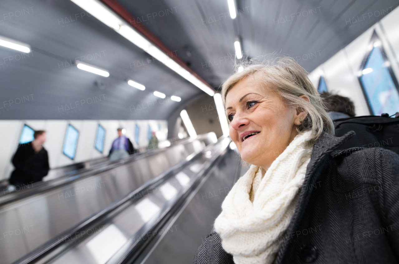 Beautiful senior woman in black coat and white woolen scarf standing at the escalator in Vienna subway