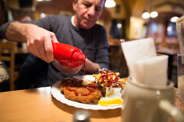 Senior man in restaurant puts ketchup on fries and vienna schnitzel