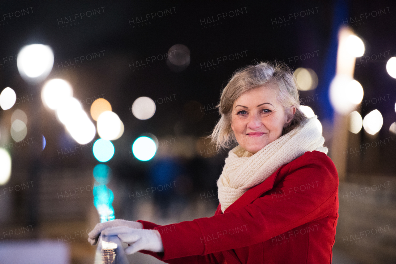 Senior woman in red winter coat and knitted scarf on a walk in illuminated night city. Vienna, Austria.