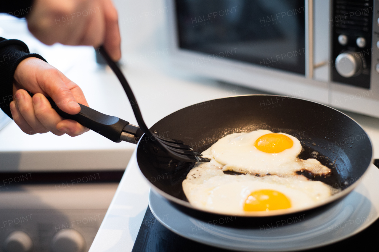 Hands of unrecognizable man preparing fried eggs for breakfast, turning them upside down with plastic spatula. Close up.