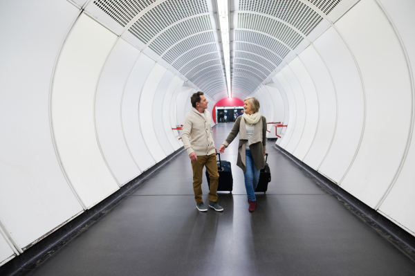 Beautiful senior couple walking in the hallway of subway in Vienna pulling a trolley luggage.