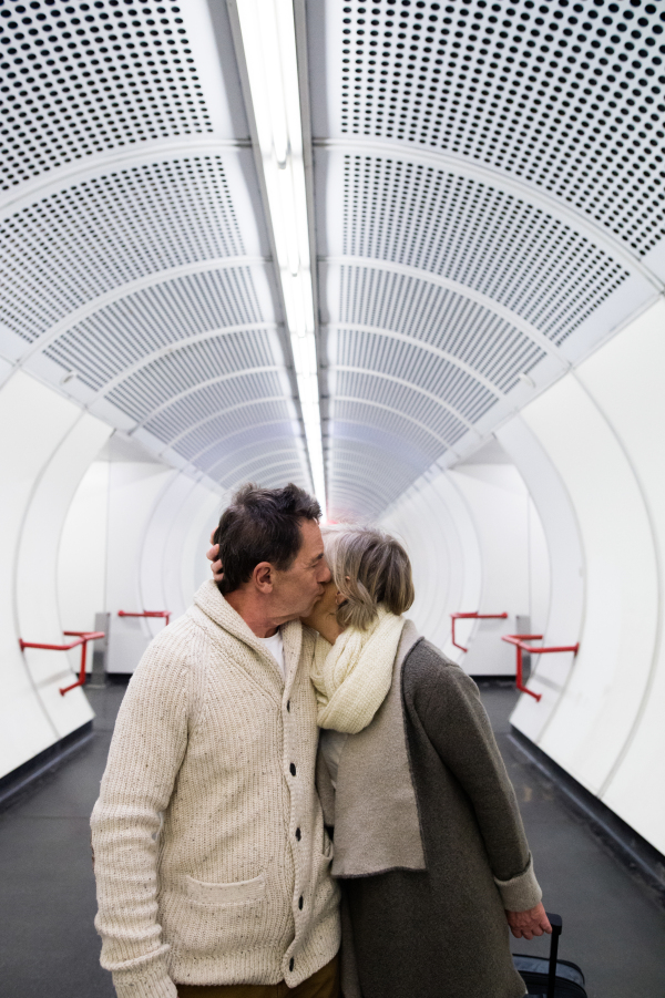 Beautiful senior couple walking in the hallway of subway in Vienna pulling a trolley luggage, kissing.