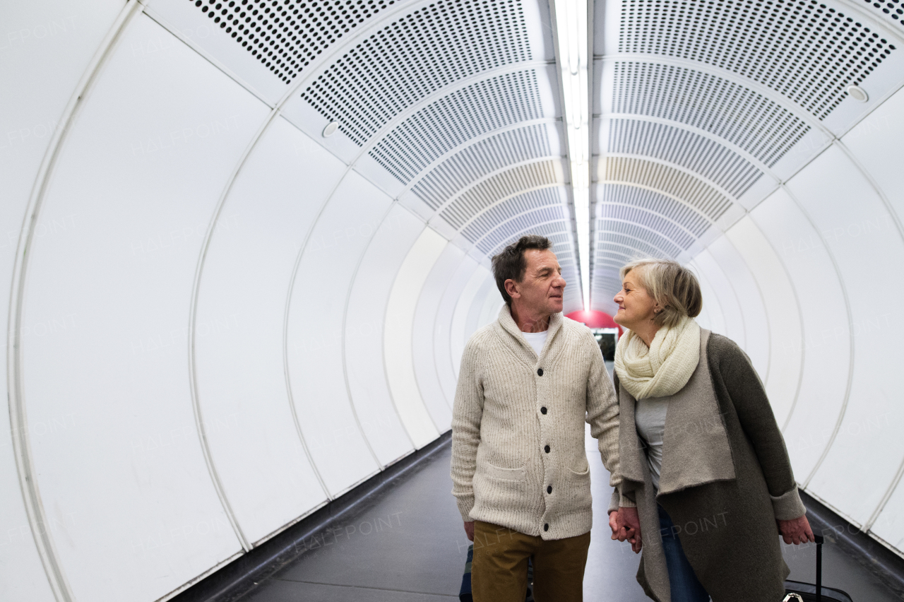 Beautiful senior couple walking in the hallway of subway in Vienna pulling a trolley luggage.