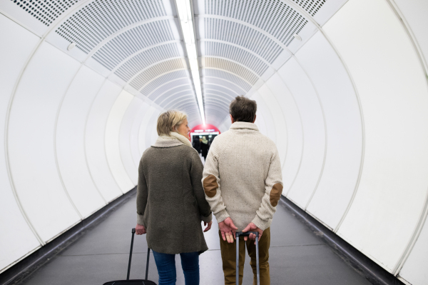 Beautiful senior couple walking in the hallway of subway in Vienna pulling a trolley luggage. Rear view.