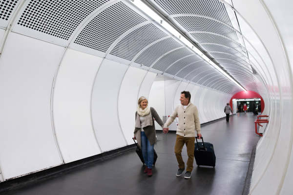 Beautiful senior couple walking in the hallway of subway in Vienna pulling a trolley luggage.