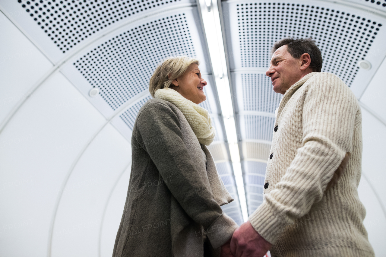 Beautiful senior couple in the hallway of subway in Vienna, facing each other, holding hands