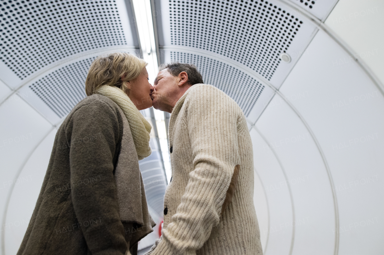 Beautiful senior couple walking in the hallway of subway in Vienna pulling a trolley luggage, kissing.