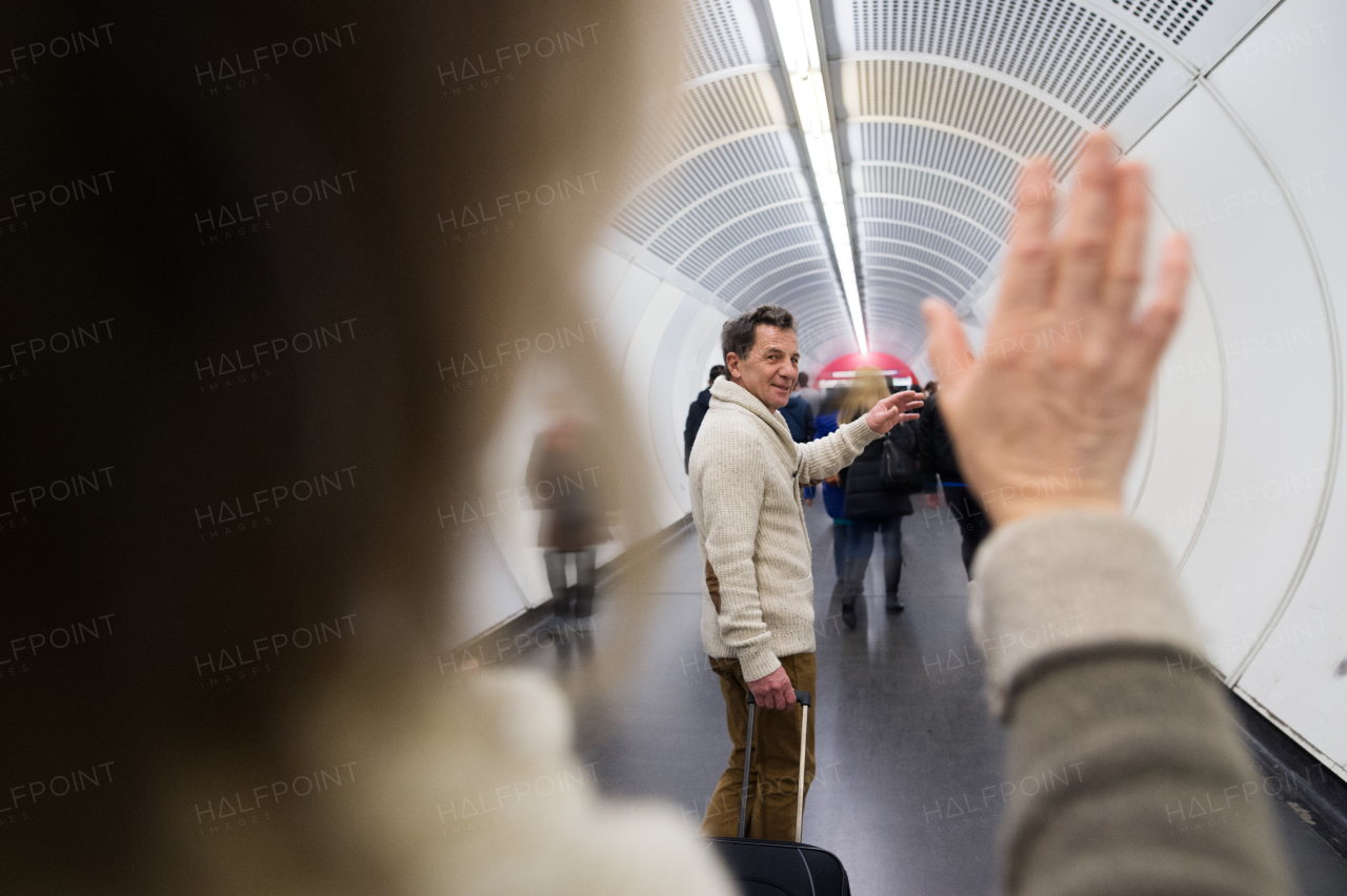 Beautiful senior couple in the hallway of subway in Vienna saying goodbye. Man pulling a trolley luggage.