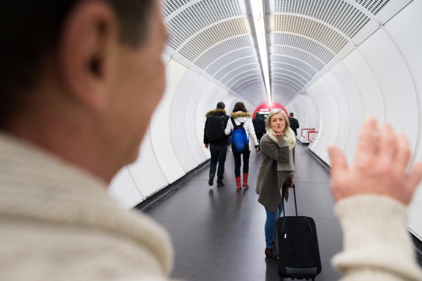 Beautiful senior couple in the hallway of subway in Vienna saying goodbye. Woman sending man a kiss and pulling a trolley luggage.