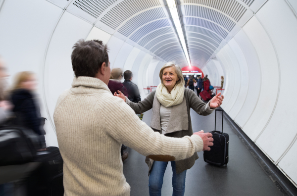 Beautiful senior couple walking in the hallway of subway in Vienna pulling a trolley luggage.