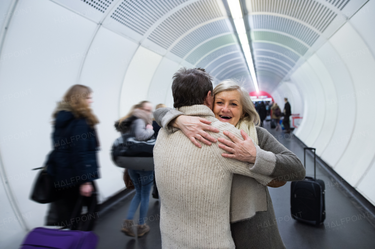 Beautiful senior couple in winter clothes in the hallway of subway in Vienna hugging. Man welcoming his wife.