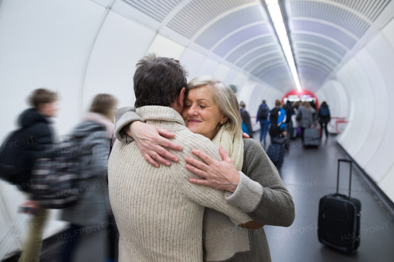 Beautiful senior couple in winter clothes in the hallway of subway in Vienna hugging. Man welcoming his wife.