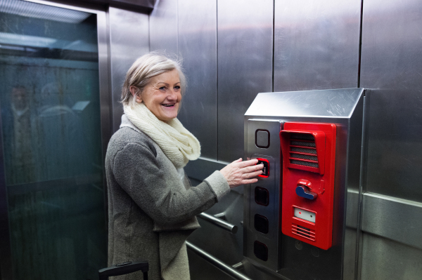 Beautiful senior woman standing in modern elevator, pushing the button. People travelling.