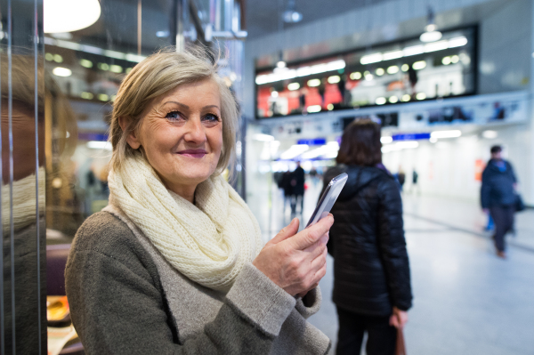 Beautiful senior woman in the hallway of subway in Vienna, holding a smart phone, texting