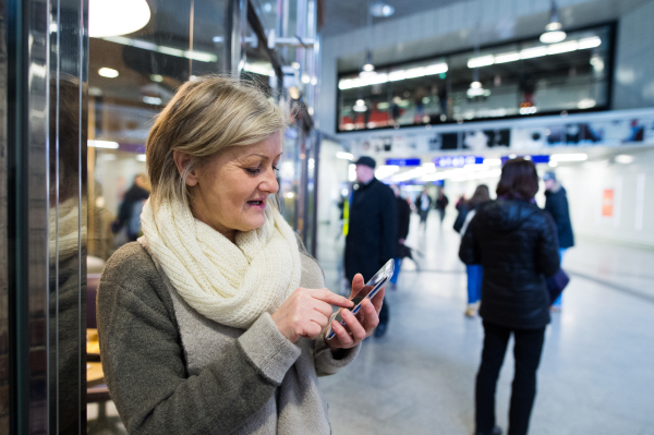 Beautiful senior woman in the hallway of subway in Vienna, holding a smart phone, texting