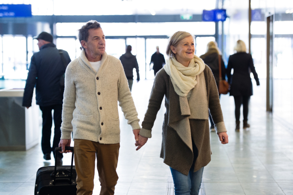 Beautiful senior couple walking in the hallway of subway in Vienna pulling a trolley luggage.