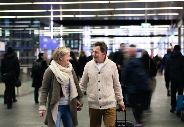 Beautiful senior couple walking in the hallway of subway in Vienna pulling a trolley luggage.