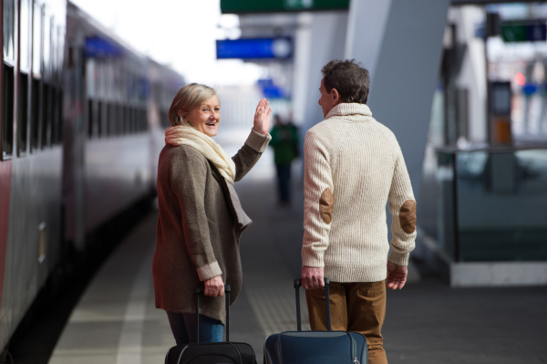 Beautiful senior couple on trainstation pulling a trolley luggage. Rear view.