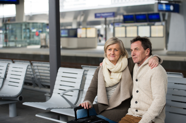 Beautiful senior couple waiting on train station, sitting on bench, looking at watch.