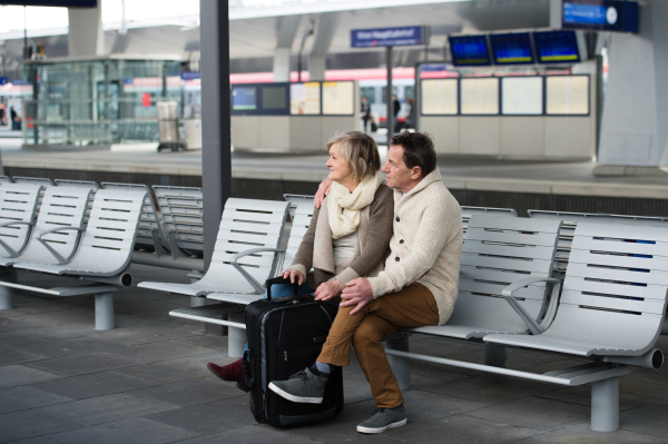 Beautiful senior couple waiting on train station, sitting on bench, looking at watch.