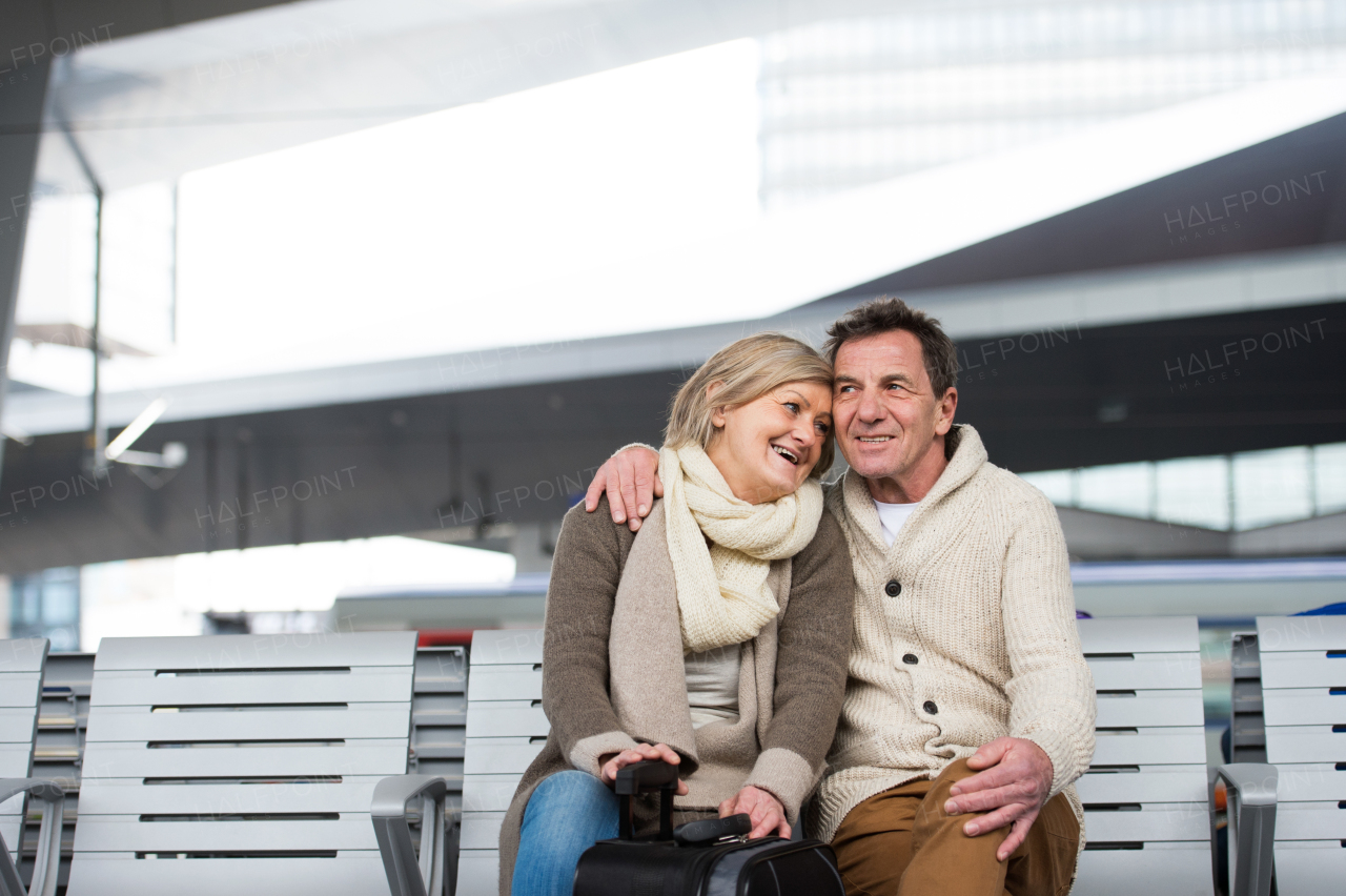 Beautiful senior couple waiting on train station, sitting on bench, hugging