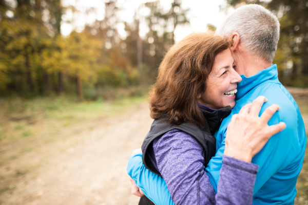 Beautiful active senior runners hugging outside in sunny autumn forest