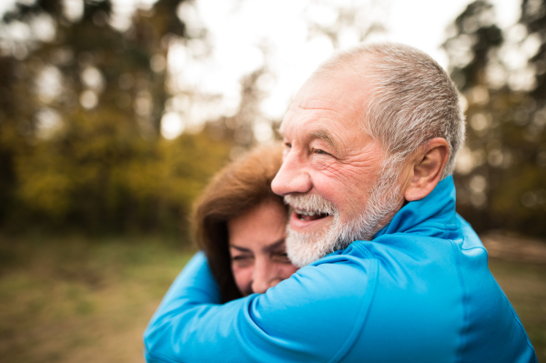 Beautiful active senior runners hugging outside in sunny autumn forest