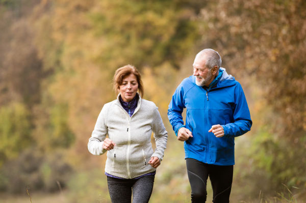 Beautiful active senior couple running together outside in sunny autumn forest