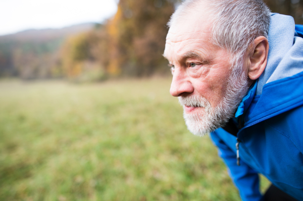 Close up of senior runner in nature. Man in blue sweatshirt, resting, smiling.